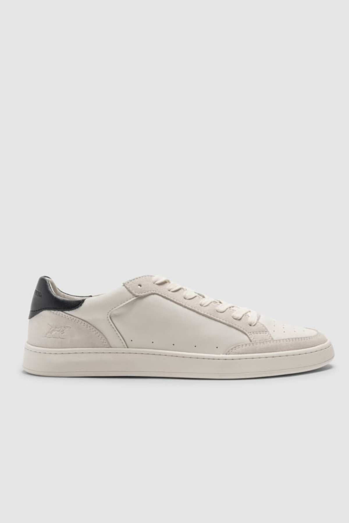 The Rodd & Gunn Sussex Street Sneaker is a white leather-lined low-top with a black heel tab, white laces, and minimal perforation details, shown on a light gray background.