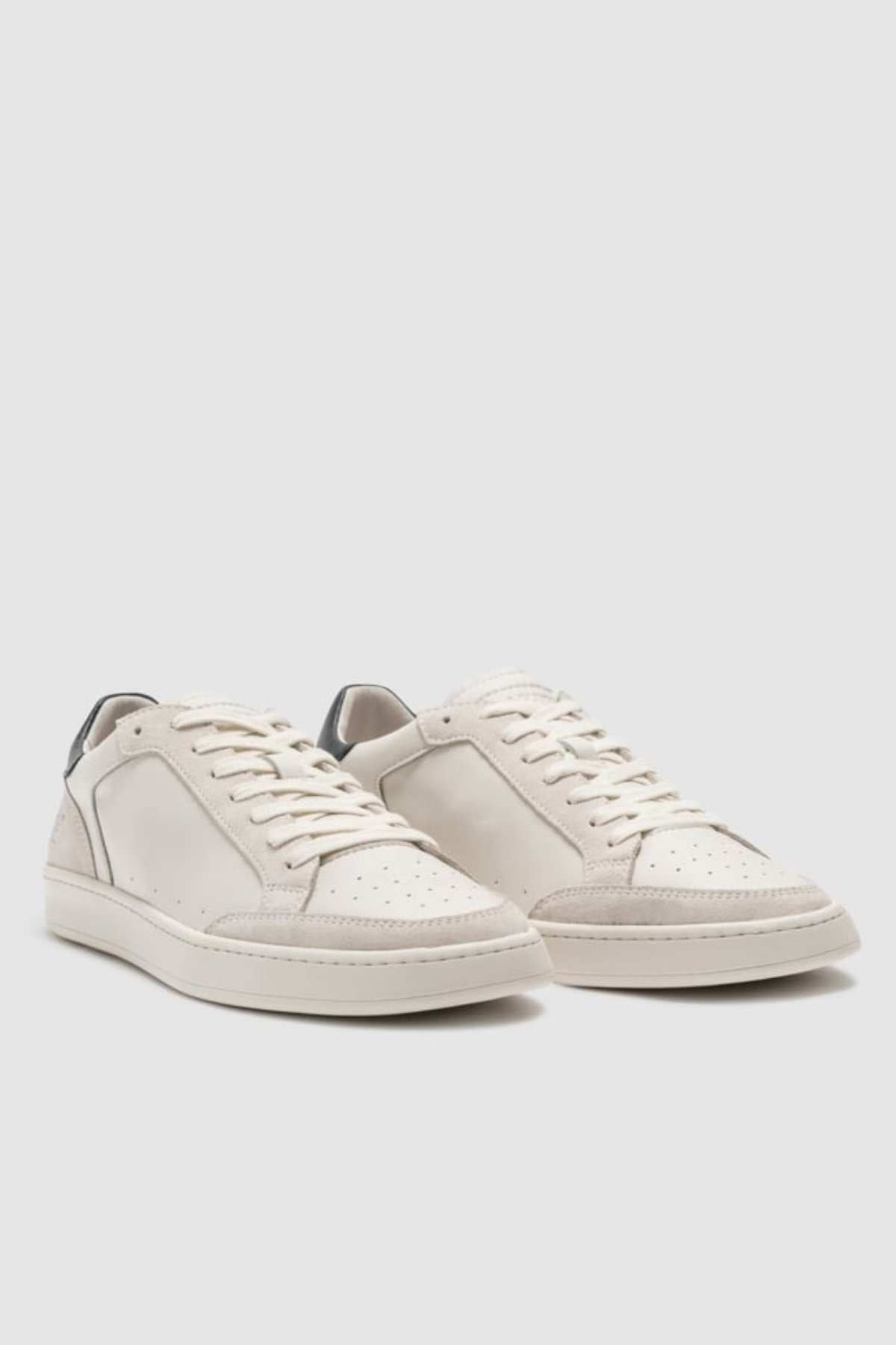 The Rodd & Gunn Sussex Street Sneaker is a white low-top with lace-up fronts, perforated toe boxes, subtle gray heel accents, and a durable rubber outsole, shown on a light gray background.