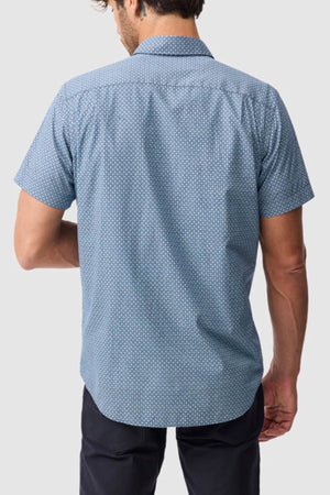 A man is seen from behind wearing the Rodd & Gunn Chartwell Sports Fit Shirt, a light blue slim fit with a small white geometric pattern, paired with dark pants against a plain light gray background.