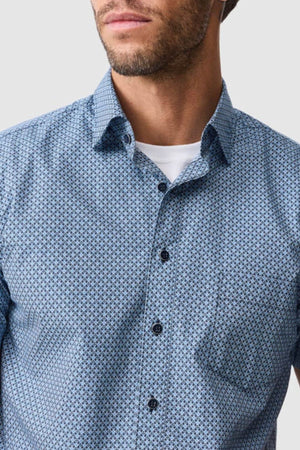 A man wears the Rodd & Gunn Chartwell Sports Fit Shirt, a light blue patterned 100% cotton top, over a white undershirt. Only his lower face and upper torso appear against a plain background.