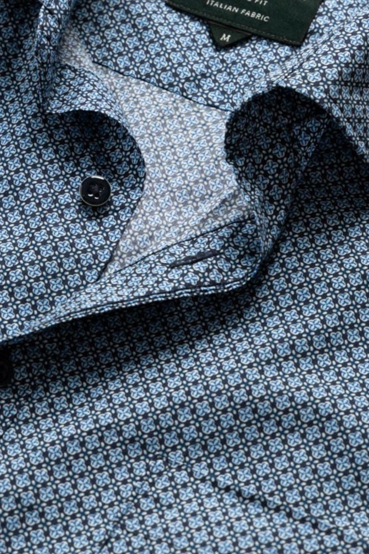 A close-up of the Rodd & Gunn Chartwell Sports Fit Shirt in blue patterned fabric with small geometric designs, partially unbuttoned to reveal a label reading "ITALIAN FABRIC" and the size "M.