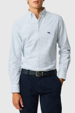 A person wears the Rodd & Gunn Gunn Check Oxford 3 Sports Fit Shirt, featuring a blue grid pattern, tucked into dark navy pants with a black belt. The Australian cotton shirt stands out against a plain light background.