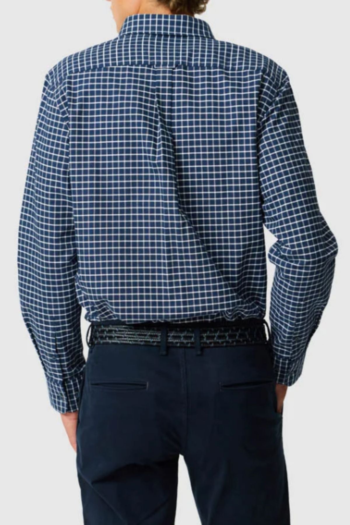 Seen from behind, a person wears the Rodd & Gunn Gunn Check Oxford 3 Sports Fit Shirt in blue and white checks, tucked into dark trousers with a black belt, against a plain light background.