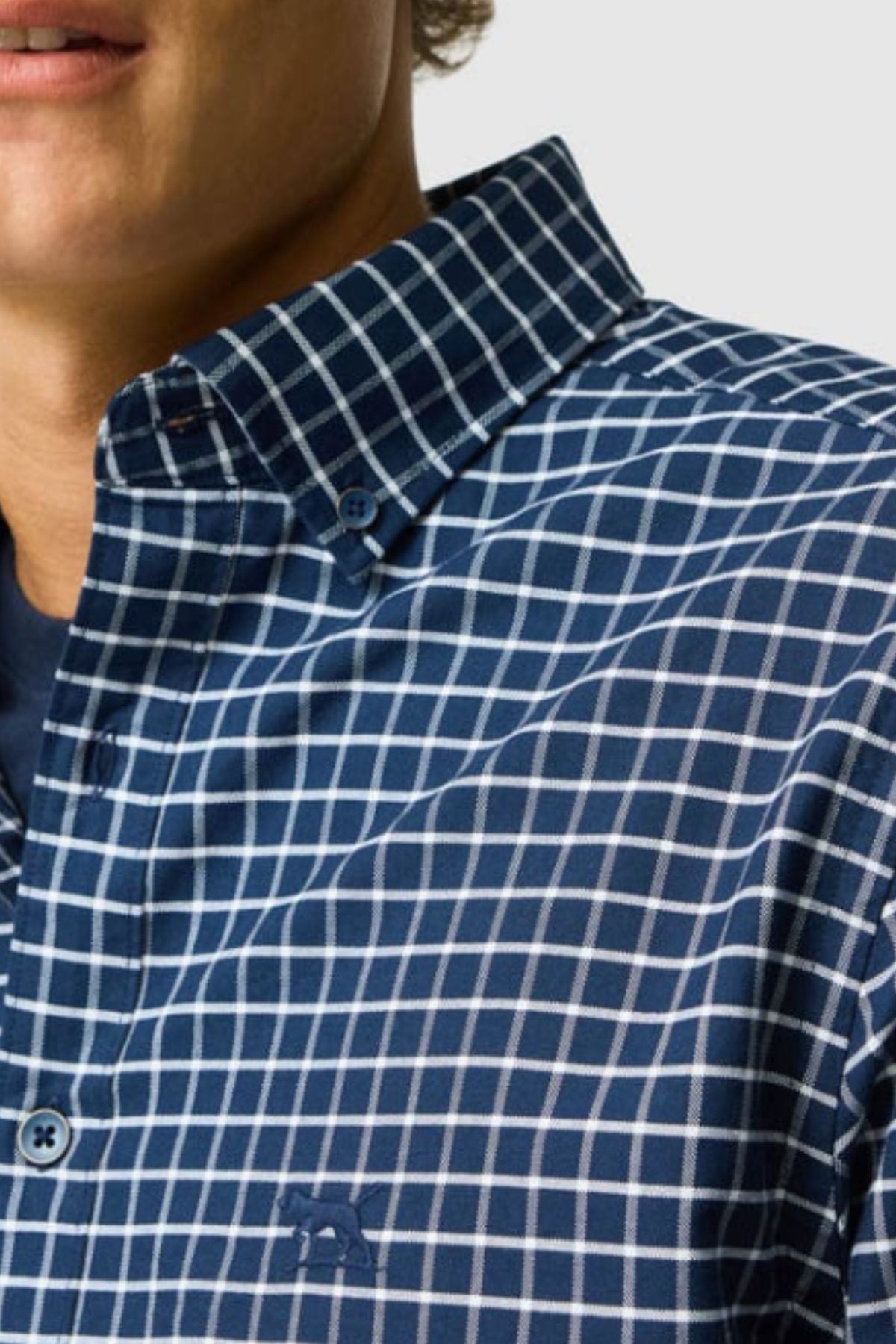 A close-up shows the lower face and upper torso of a person wearing the Rodd & Gunn Gunn Check Oxford 3 Sports Fit Shirt, a blue Australian cotton shirt with a white checkered pattern, highlighting its sports fit.