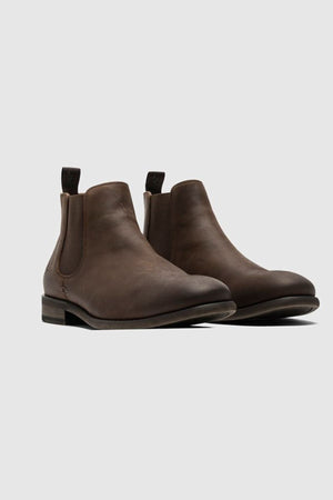 The Rodd & Gunn Ealing Chelsea Boot, crafted from brown oiled leather with elastic side panels, pull tabs, and a flexible rubber outsole, is displayed against a light gray background.