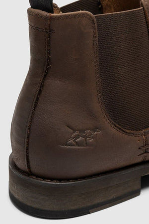 Close-up of the Rodd & Gunn Ealing Chelsea Boot’s heel and side in brown oiled leather, featuring an elastic panel, detailed stitching, a small embossed camel logo by the heel, and a flexible rubber outsole for comfort.