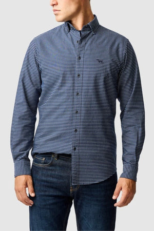 A man wearing the Rodd & Gunn Gunn Check Oxford 5 Sports Fit Shirt with long sleeves and dark blue jeans stands against a light gray background, looking to his left.