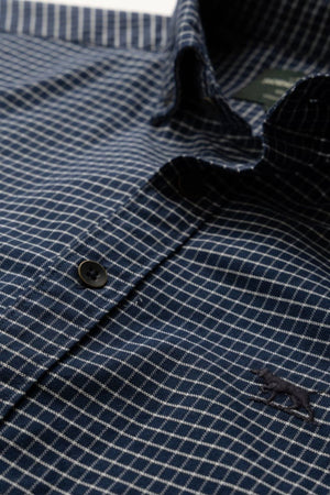 A close-up of the Rodd & Gunn Gunn Check Oxford 5 Sports Fit Shirt shows blue checkered fabric with white lines, dark buttons, and a small embroidered animal logo, crafted from premium Italian fabric for a tailored sports fit.