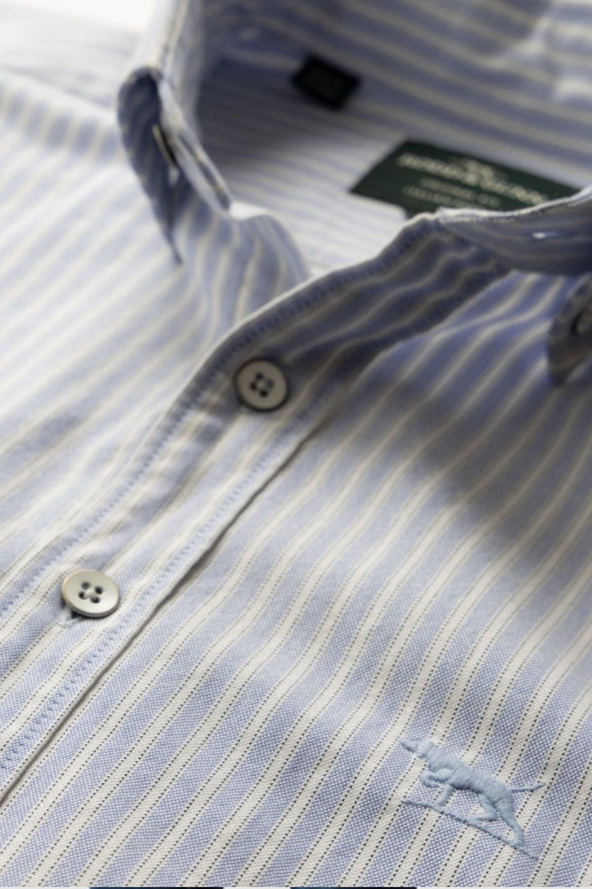 Close-up of the Rodd & Gunn Gunn Oxford Stripe 4 Of Shirt in light blue and white, made from pre-washed cotton, featuring white buttons and an embroidered horse logo on the chest.