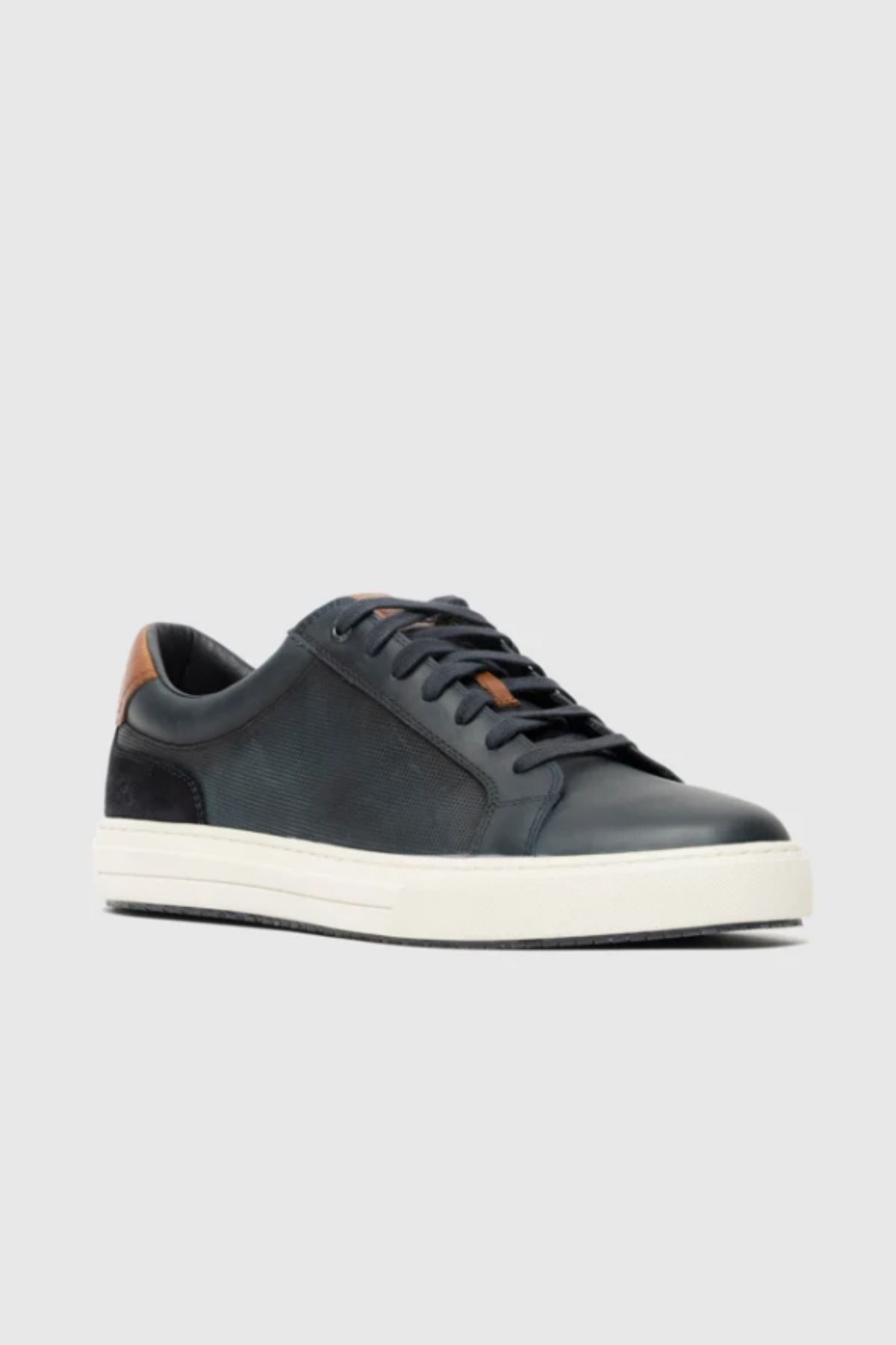 The Rodd & Gunn Transit Sneaker is a black low-top leather sneaker with black laces, a white rubber sole, and a brown heel accent, shown against a plain light gray background.