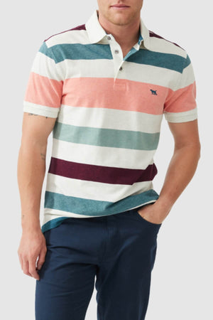A man wears a Rodd & Gunn Cambridge Sports Fit Polo, featuring wide horizontal stripes in teal, coral, white, burgundy, and light blue (USA-grown cotton), paired with dark blue pants. His left hand rests in his pocket.