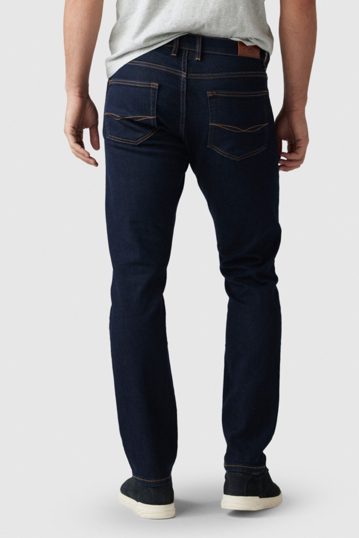 A person in a grey t-shirt, black shoes, and Rodd & Gunn Fanshawe Straight Jeans stands with their back to the camera against a plain light background.