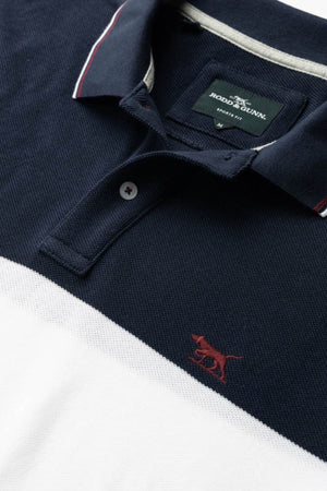 Close-up of the Rodd & Gunn Homebay Polo in navy and white, featuring a red embroidered dog logo, brand label inside the collar, ribbed collar with red accents, and crafted from Australian Good Earth Cotton.