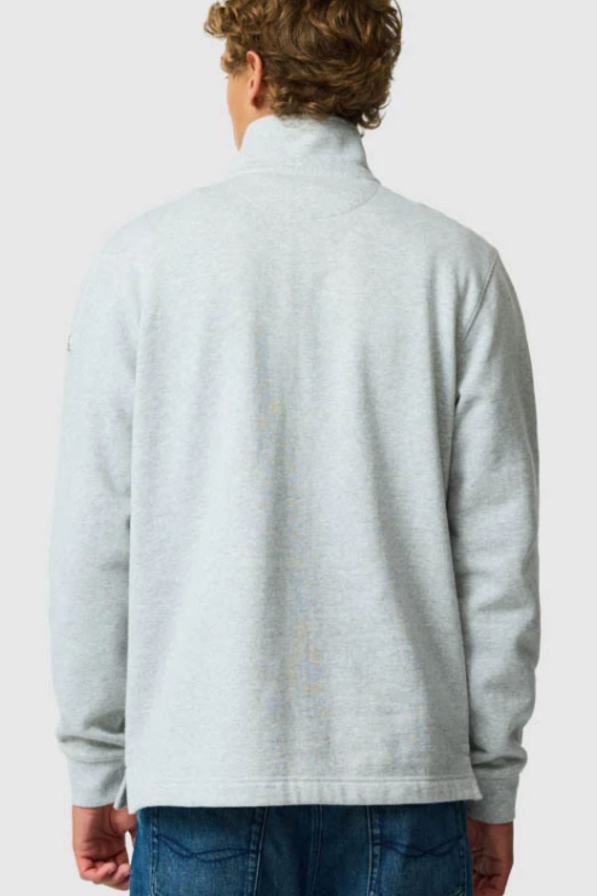 A person with curly hair is seen from behind, wearing the Rodd & Gunn Jubilee Sweat in light gray and blue jeans, standing against a plain light background.
