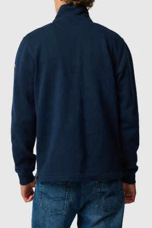 A person wearing the Rodd & Gunn Jubilee Sweat, a dark blue quarter zip jacket, and blue jeans, shown from the back against a plain light background, embodying sustainable craftsmanship.