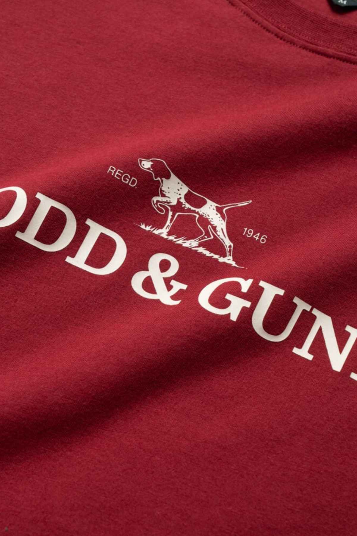 Close-up of the Rodd & Gunn Logo T-Shirt in Sports Fit shows a red design with a white dog graphic and "ODD & GUN" text, "REGD" above, and "1946" below. Made from sustainably farmed cotton, this tee offers an eco-friendly choice.