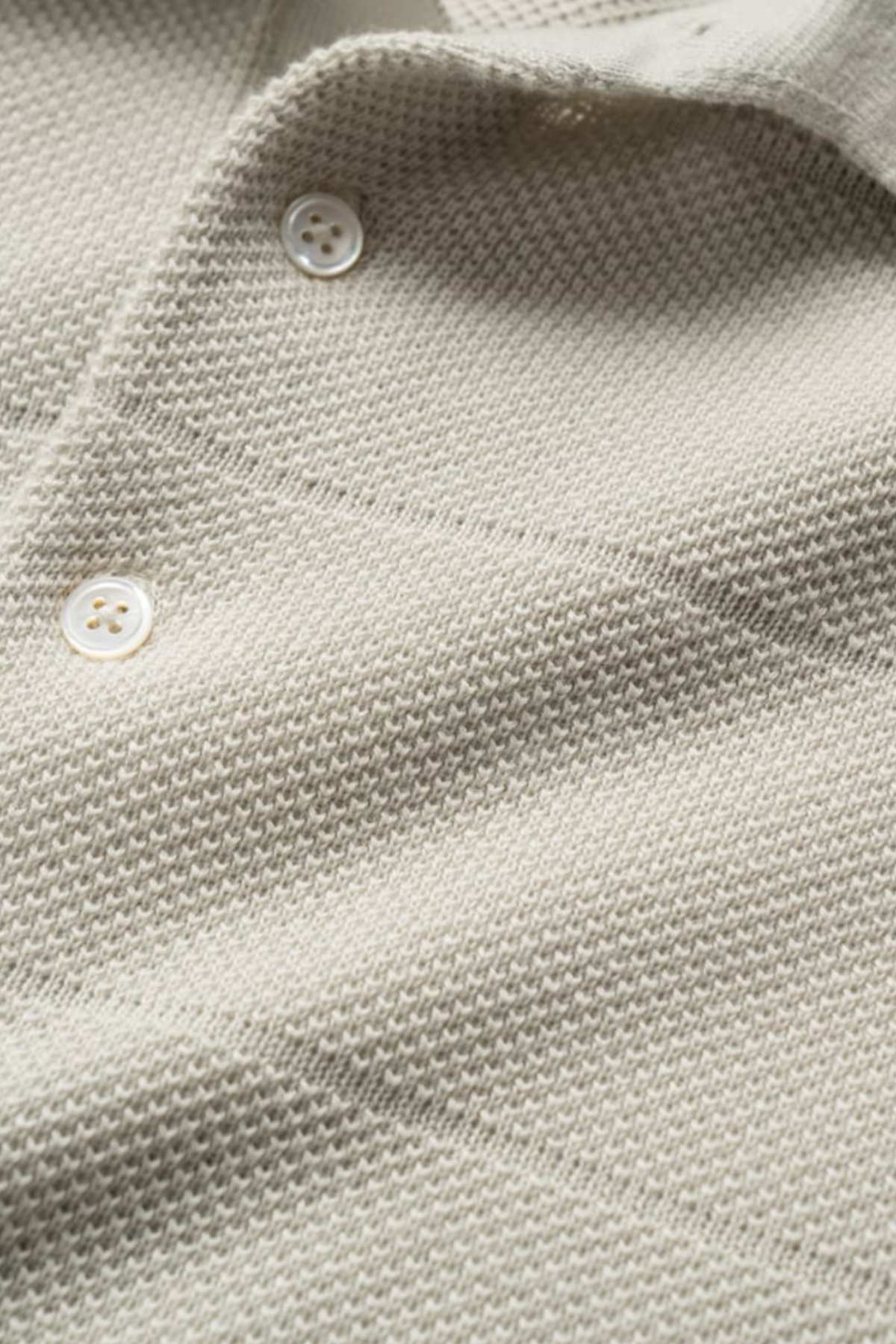 Close-up of a textured beige fabric with a classic pique stitch pattern and three white buttons. The soft, lightweight material resembles the Rodd & Gunn Masons Flat Knit, ideal for clothing such as shirts or cardigans.