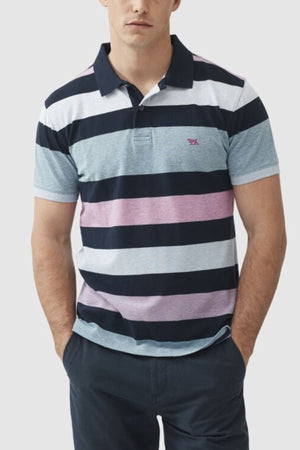 The individual wears a Rodd & Gunn Solomons Point Sports Fit Polo with short sleeves and stripes in navy, white, light blue, and pink, crafted from 100% cotton for comfort. They pair it with dark pants while posing with hands in pockets against a plain backdrop.