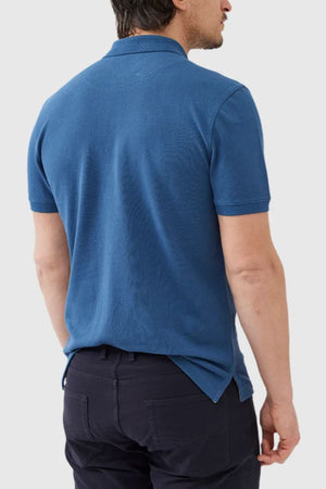 A man, seen from the back, wearing a Rodd & Gunn The Gunn Polo made from comfortable Australian Cotton. The blue short-sleeved shirt and dark pants complement his short dark hair as he stands against a plain, light-colored background.