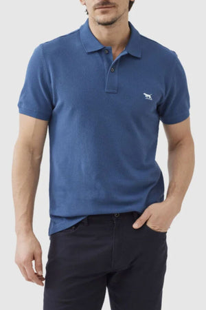 A man is wearing a Rodd & Gunn The Gunn Polo, crafted from Australian Cotton, featuring a small white embroidered animal logo on the left chest. He pairs it with dark pants. The image is taken from mid-thigh up, showcasing a relaxed yet polished casual look.