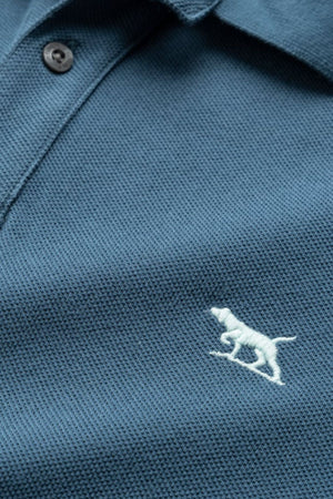 Close-up of The Gunn Polo by Rodd & Gunn in a rich dark blue shade, showcasing its textured and comfortable design. This casual polo shirt features two dark buttons near the collar and is detailed with a small, embroidered white dog logo on the left side of the chest, crafted from premium Australian Cotton.