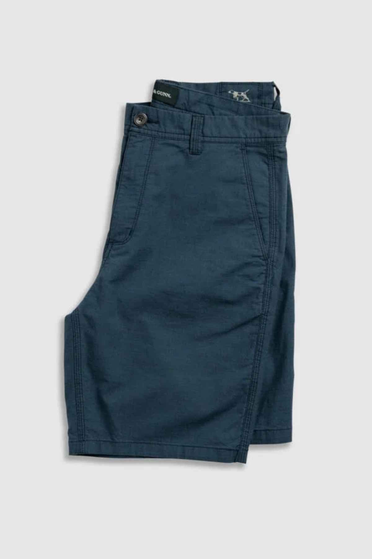 Rodd & Gunn The Gunn Short, a pair of neatly folded, dark blue men's shorts made from high-quality cotton, features front pockets, belt loops, and a button closure, showcasing their original fit against a plain white background.