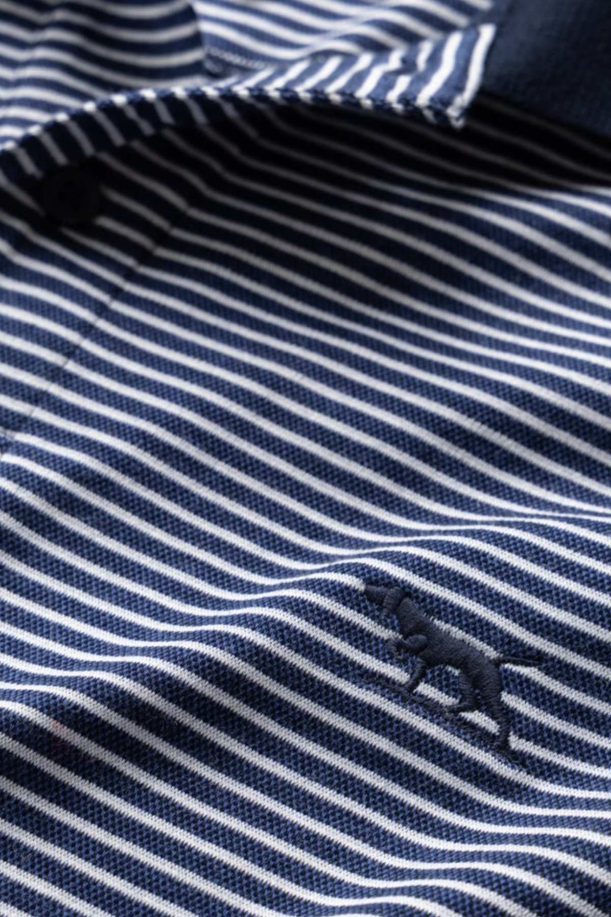 Close-up image of the blue and white striped fabric of the Rodd & Gunn Wye Creek Polo, featuring a small embroidered silhouette of an elephant. The fabric appears to be part of a polo shirt, with visible collar and button details.