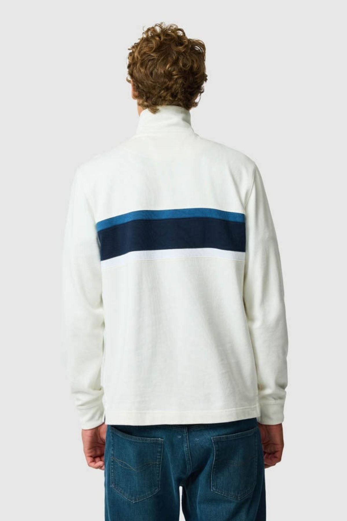 A person with curly hair, seen from the back, wears the Rodd & Gunn Chesterfield Sweat with blue stripes and blue jeans—highlighting eco-conscious style against a plain light gray background.