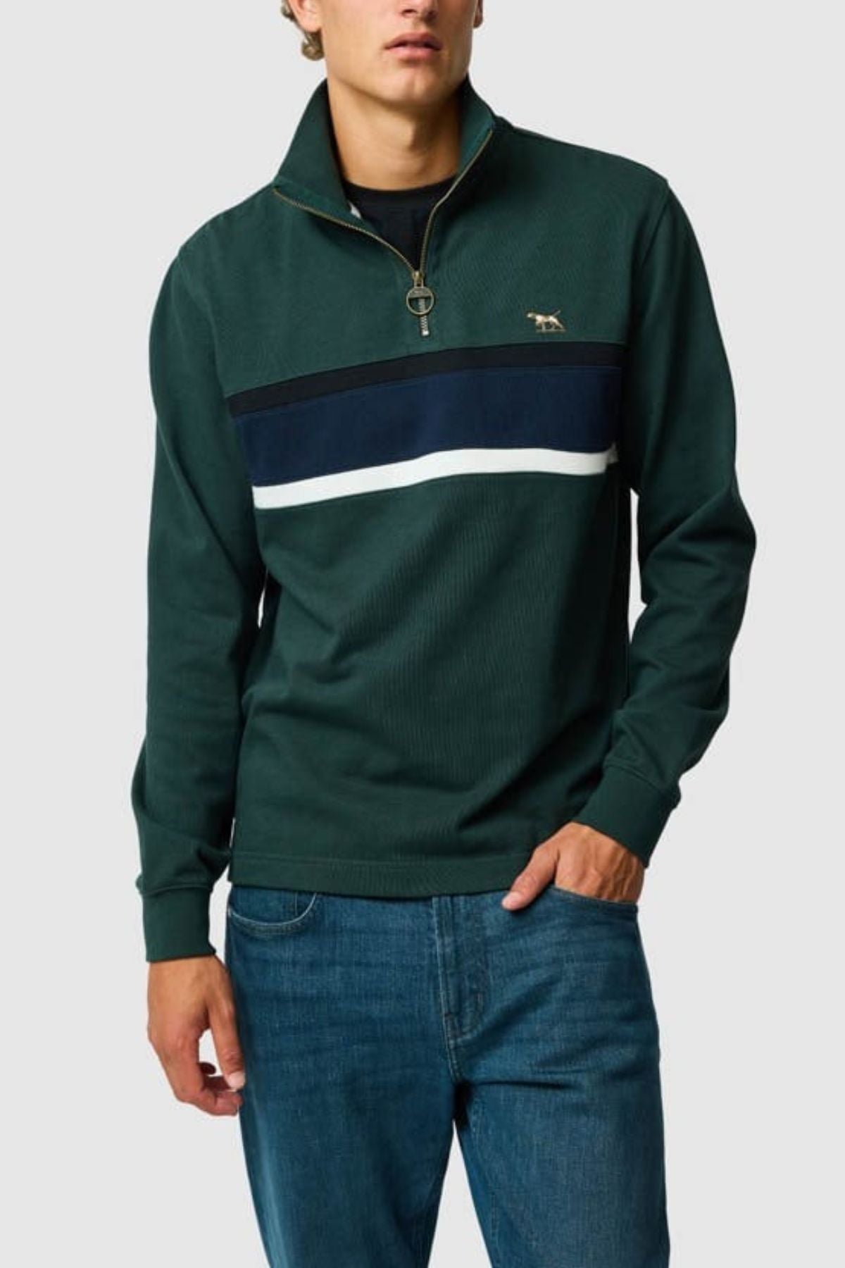 A person wears the Rodd & Gunn Chesterfield Sweat—a dark green quarter-zip pullover with navy and white chest stripes, crafted from Good Earth Cotton—styled with blue jeans and set against a plain light background.