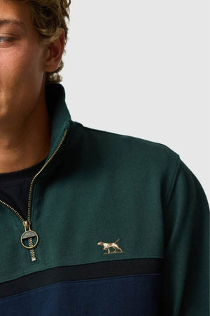 A close-up of a person wearing the Rodd & Gunn Chesterfield Sweat, a dark green and navy zip-up sweater with an embroidered dog logo, made from Good Earth Cotton for eco-conscious style; only their lower face and upper torso are shown.