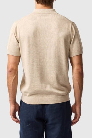 A man wearing the Rodd & Gunn Brooklands Knit, a beige Australian cotton short-sleeve shirt, and dark blue pants is shown from the back against a plain light gray background.
