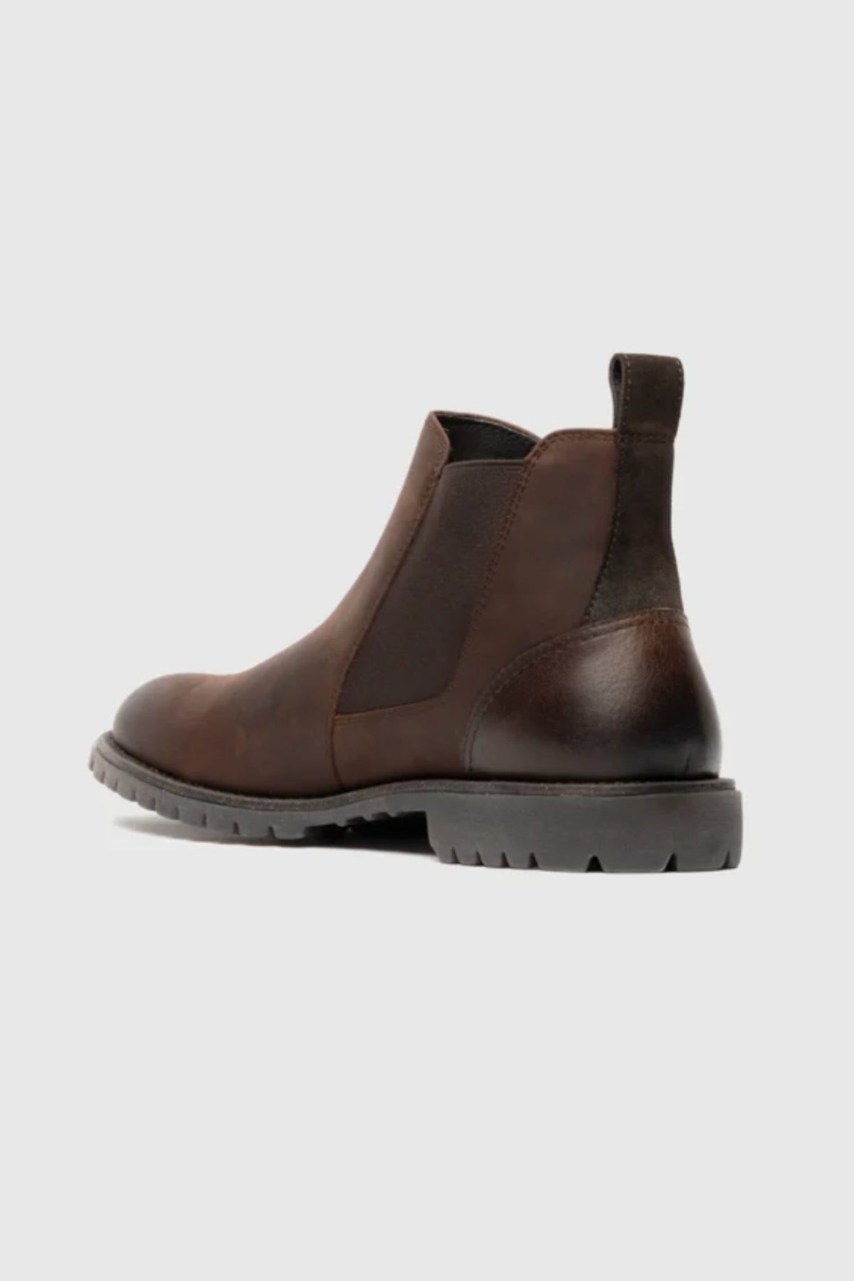 The Rodd & Gunn Clearmont Chelsea Boot is shown from a rear side angle in dark brown leather, featuring elastic side panels, a heel pull tab, and a rugged black sole, displayed on a light gray background.