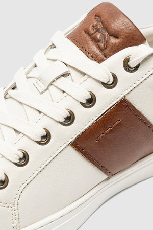 Close-up of the Rodd & Gunn Endeavour Cruise Sneaker, featuring comfortable leather construction, brown accents, metal eyelets, white laces, and an embossed logo on a brown patch near the ankle.