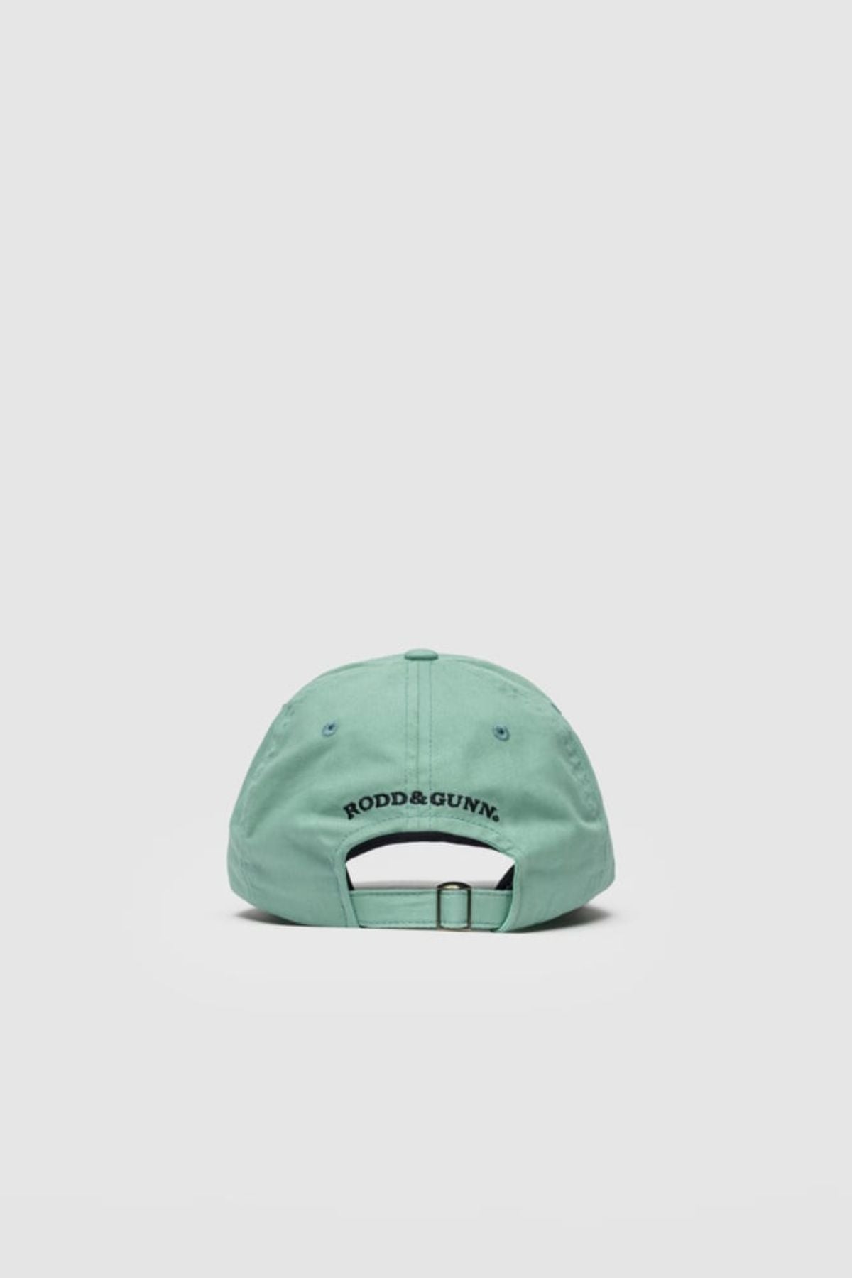 The Rodd & Gunn Gunn Cap is a light green cotton twill cap shown from the back, with the "RODD & GUNN" logo embroidered in black above an adjustable strap. Set against a plain light gray background, it delivers a casual yet polished style.
