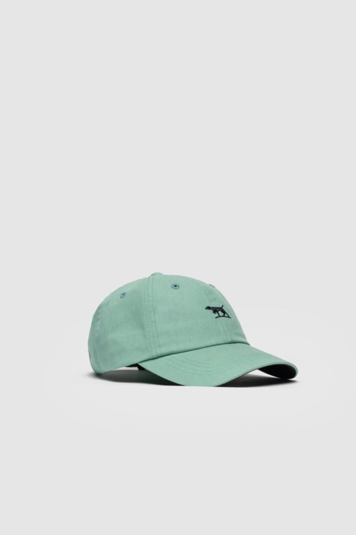 The Rodd & Gunn Gunn Cap is a light green cotton twill hat featuring a small black dog embroidered on the front, shown against a plain light gray background.