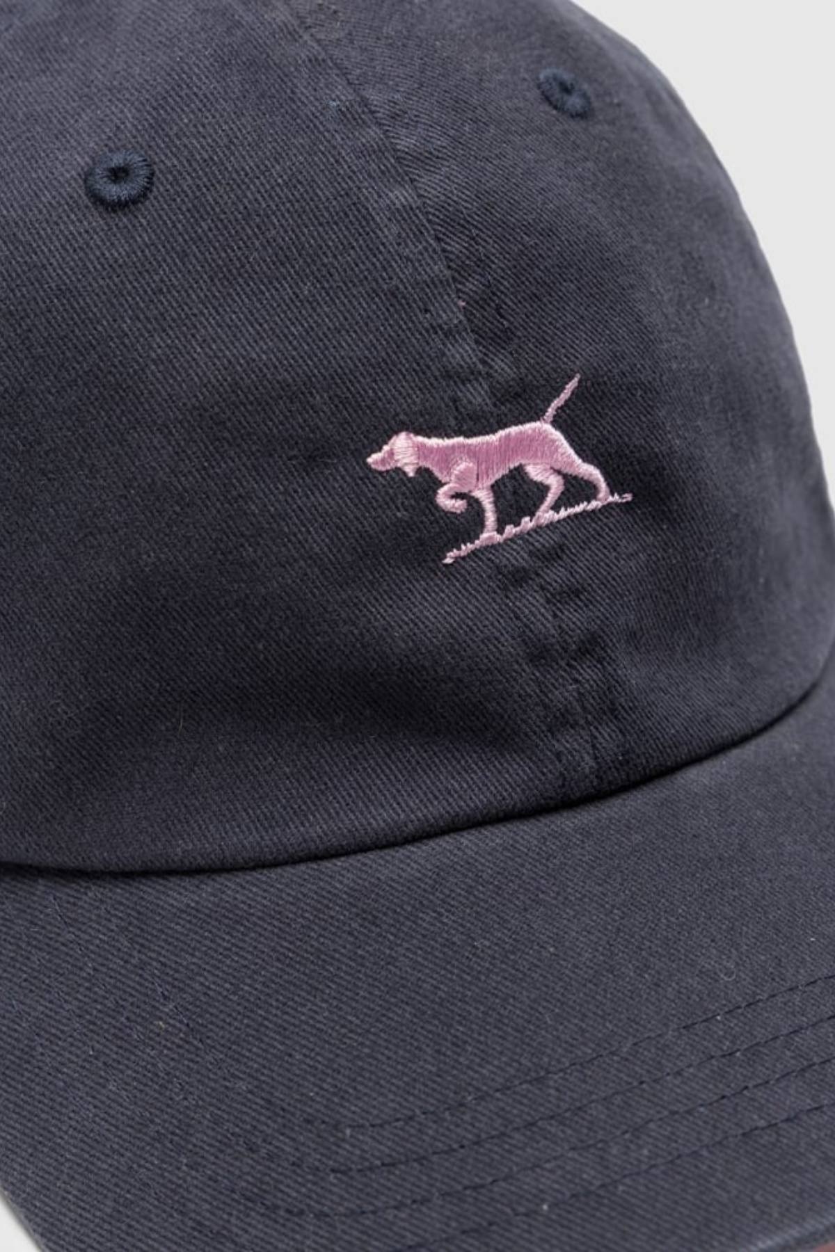 The Rodd & Gunn Gunn Cap Petite is a navy blue cotton twill cap with a small pink embroidered dog on the front and an adjustable back strap for a comfortable fit.