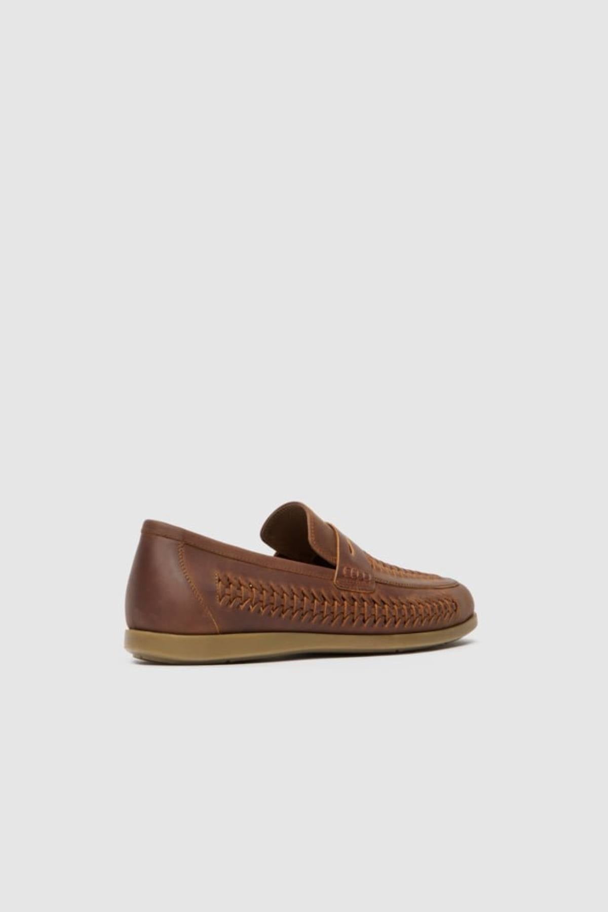 The Rodd & Gunn Gisbourne Huarache Slip On is a brown leather loafer with woven side detailing, a low heel, and a tan rubber sole—perfect breathable summer shoes shown against a plain light gray background.