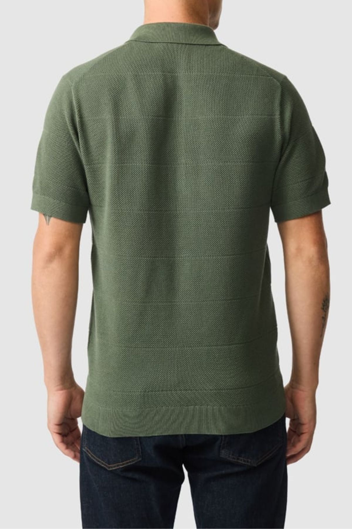 A person is shown from the back, wearing the Rodd & Gunn Masons Flat Knit short-sleeved green polo and dark jeans, standing against a plain light gray background.