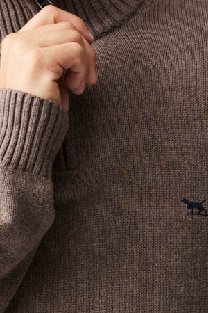 A close-up of a person wearing the Rodd & Gunn Merrick Bay Knit sweater, made from 100% cotton jersey knit with ribbed cuffs and high collar, holding the collar. A small dark animal logo is embroidered on the chest.