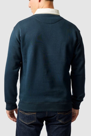 A man is seen from behind wearing the Rodd & Gunn Otago Sweat over a collared shirt and blue jeans, standing against a light gray background.