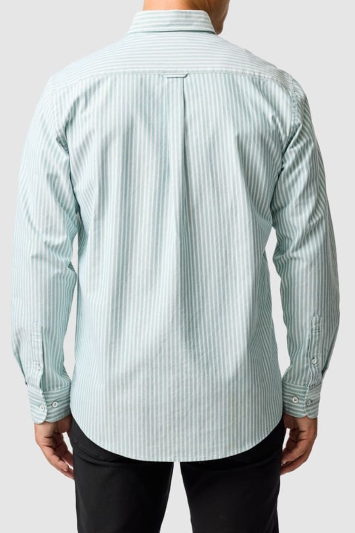 A man is seen from behind wearing the Rodd & Gunn Gunn Oxford Stripe 4 Of Shirt, a long-sleeved, light blue and white Oxford stripe shirt with back pleat, buttoned cuffs, and paired with black pants for a classic look.