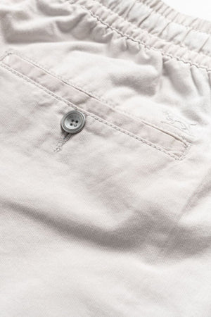 Close-up of the Rodd & Gunn Resort Short in light beige, showcasing an elastic waistband, back pocket with single button closure, soft cotton fabric, and a subtle embroidered logo above the pocket.