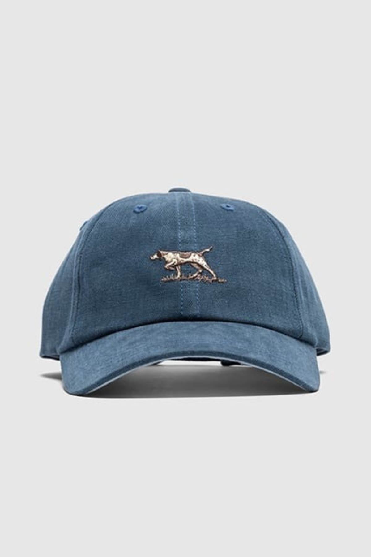 The Rodd & Gunn Signature Cap is a blue cotton twill hat with an embroidered brown and white dog walking, centered on the front, set against a plain light gray background.