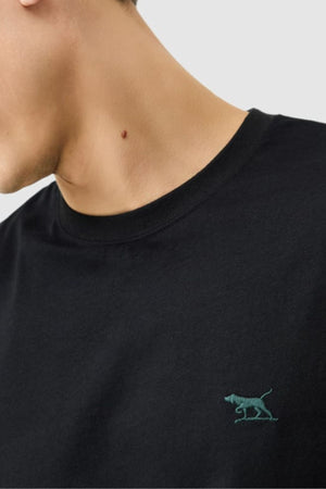 A person wearing the Rodd & Gunn The Gunn Tee 2.0 in black, featuring a small green embroidered dog logo on the chest; only their lower face, neck, and upper torso are visible.