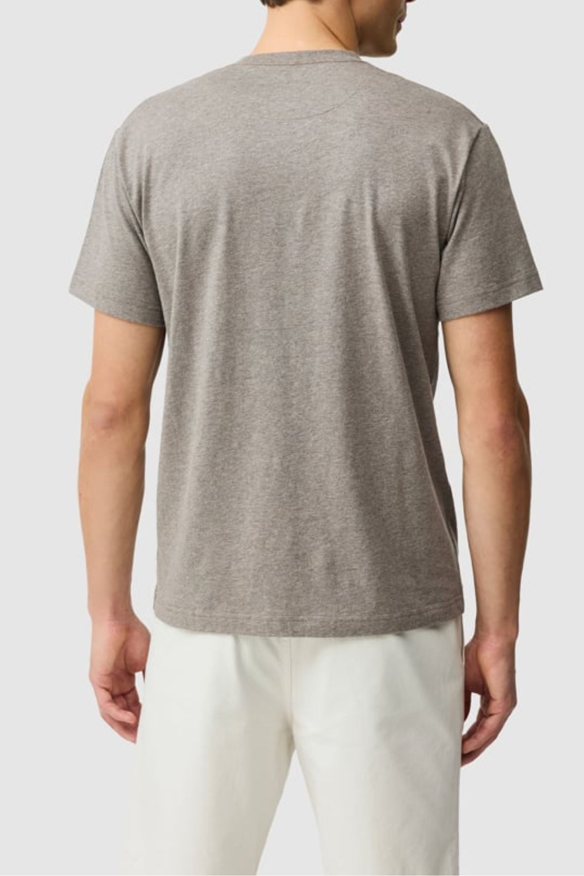A person is seen from behind, wearing a short-sleeved gray Rodd & Gunn The Gunn Tee 2.0 and white pants, standing against a plain light background.