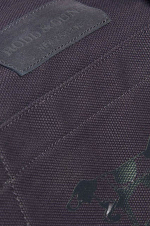 Close-up of the Rodd & Gunn Ponsonby Road Duffle Bag in dark cotton canvas, featuring visible stitching, a leather patch with a partial logo, and a subtle running dog graphic in the lower right corner.
