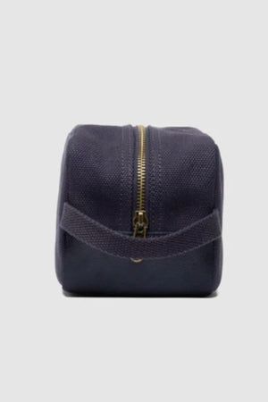 The Rodd & Gunn Ponsonby Wash Bag in navy blue cotton canvas, featuring a gold zipper and fabric handle, is displayed upright against a plain light gray background.