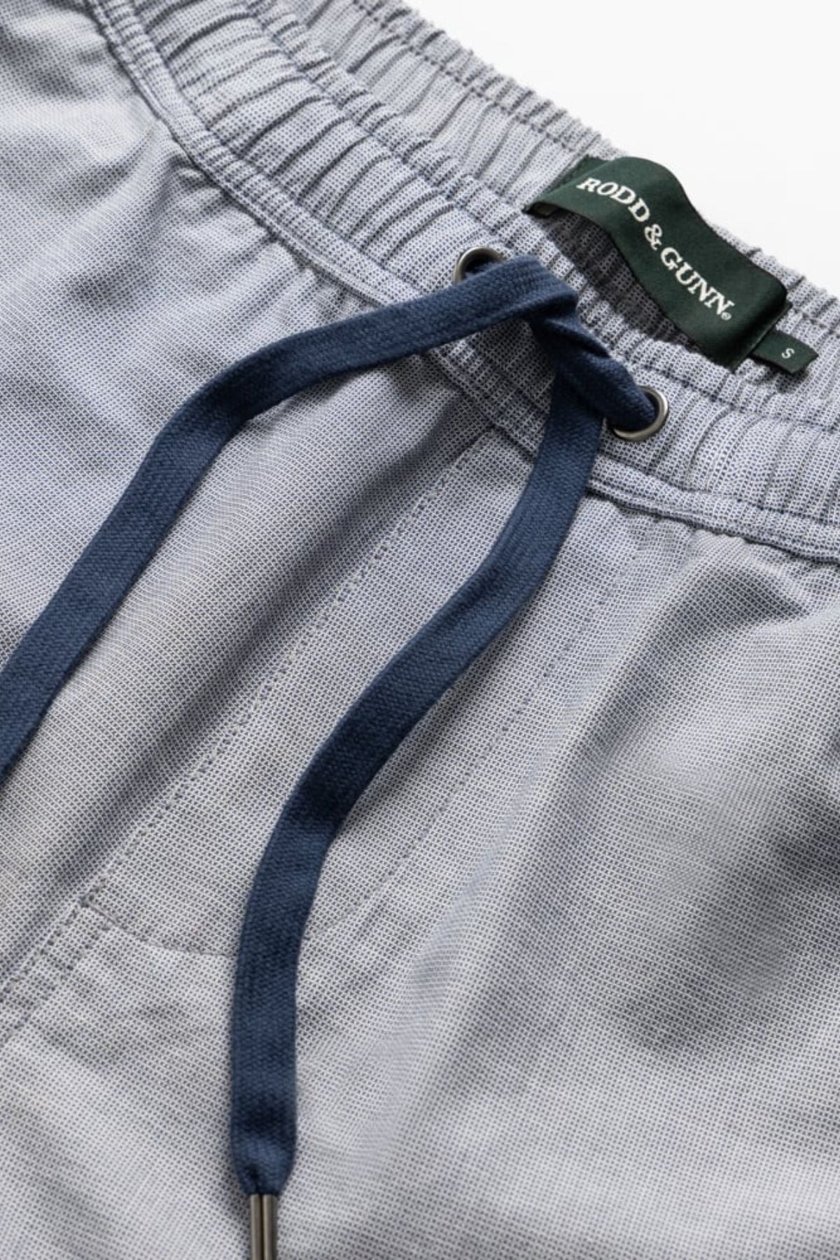 Close-up of light grey Rodd & Gunn Resort Short with an elastic waist, dark blue drawstring, front stitching, and a visible green "Rodd & Gunn" label.