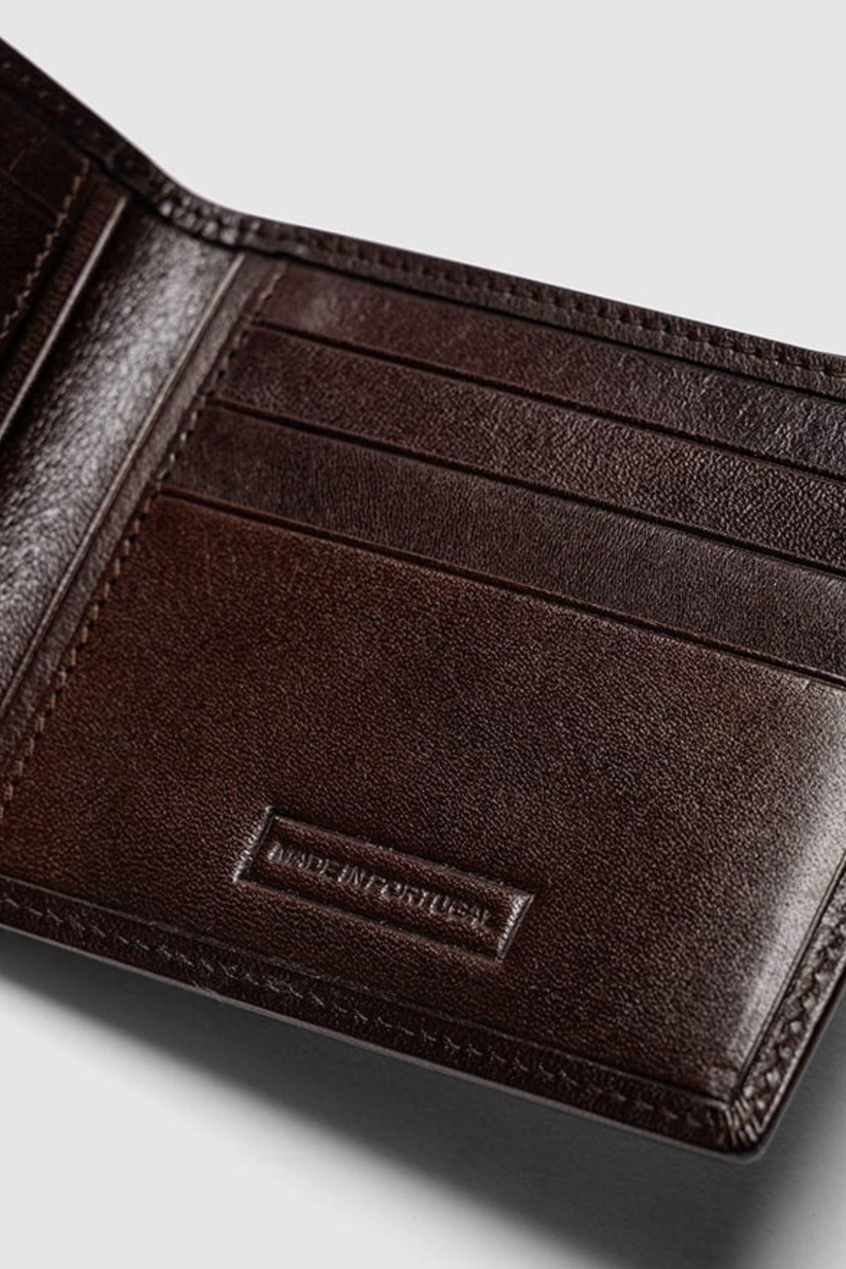 A close-up of the Rodd & Gunn Wakefield Bi-Fold Wallet in dark brown Italian leather, showcasing multiple card slots, "MADE IN PORTUGAL" embossing inside, and built-in RFID protection.