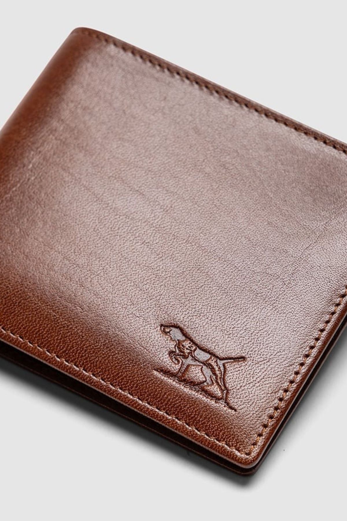 The Rodd & Gunn Wakefield Bi-Fold Wallet is crafted from brown Italian leather, features stitched edges and an embossed dog in the corner, and is displayed against a plain light background.